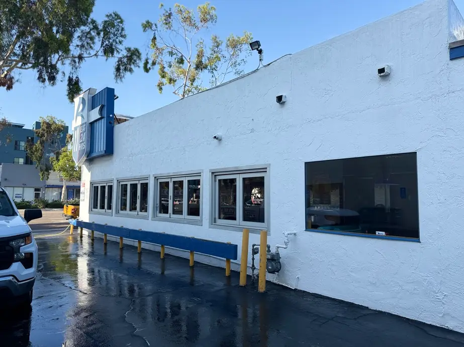 Restaurant frontage and parking lot after a wash, wet asphalt under a blue sky